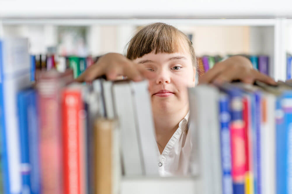 a person fixing books on a shelf, viewed from the other side of the shelf