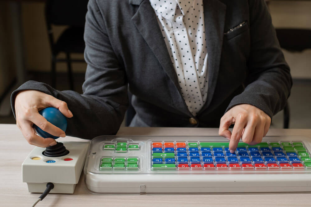 close up of a person using an accessible keyboard and joystick mouse