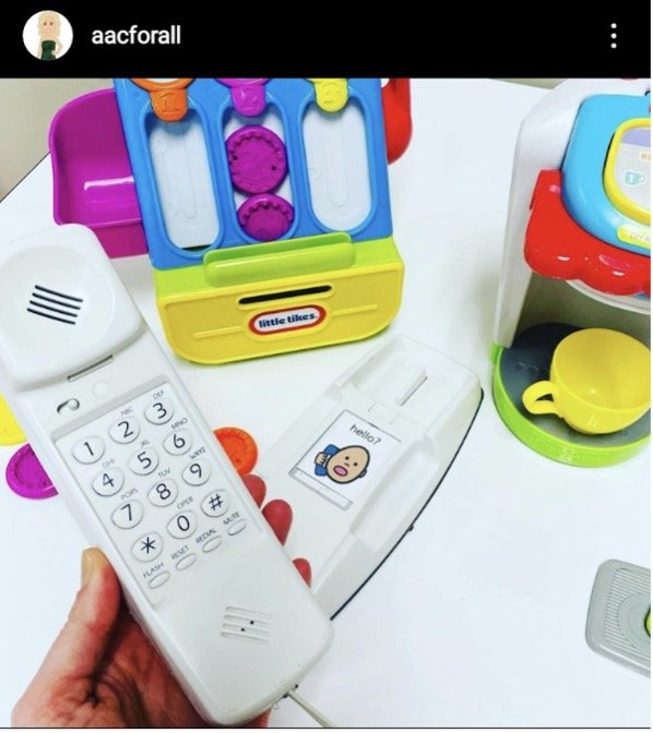 Instagram post by aacforall showing a hand picking up a phone. An icon of someone holding a phone with the text “hello?” is visible. A play coffee maker and cash register are also visible in the background.