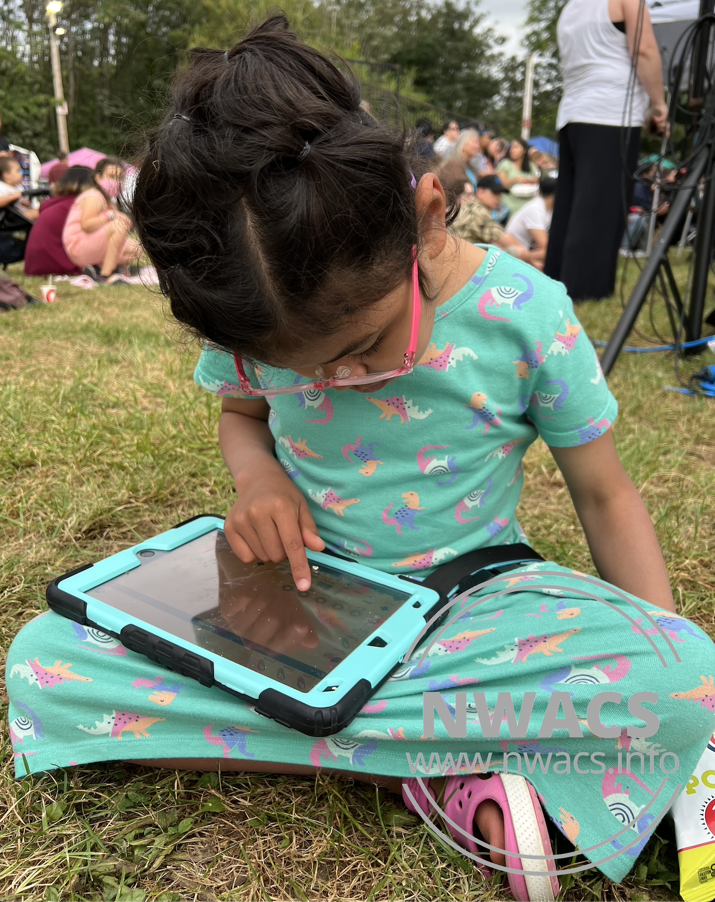 Melissa's daughter sitting out grass using her AAC device