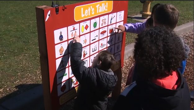 children pointing the let's talk playground communication board 