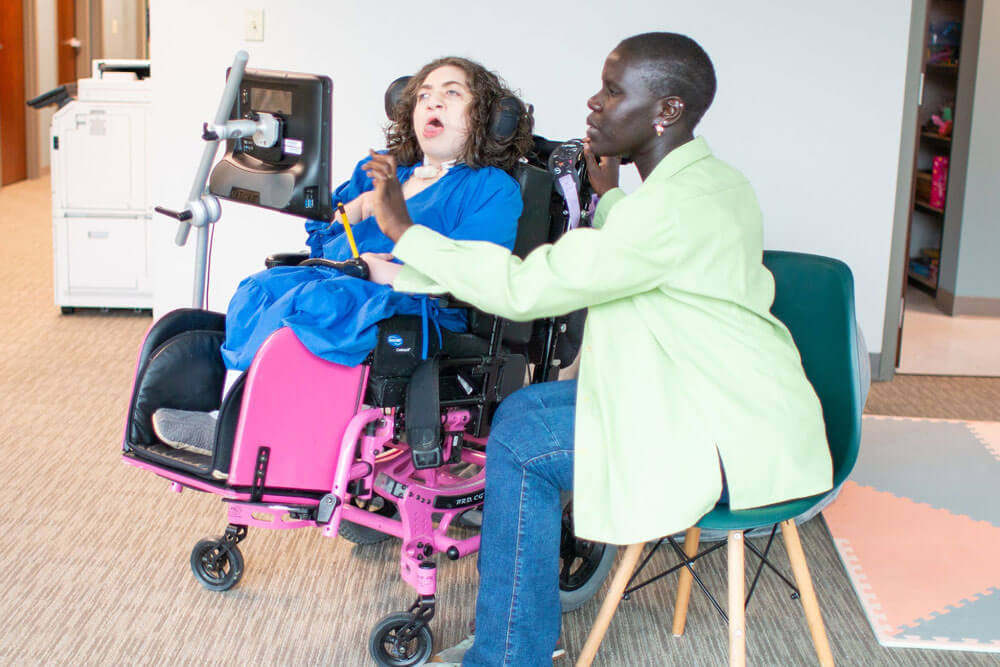 an AAC user in a wheelchair interacting with a communication partner seated next to them