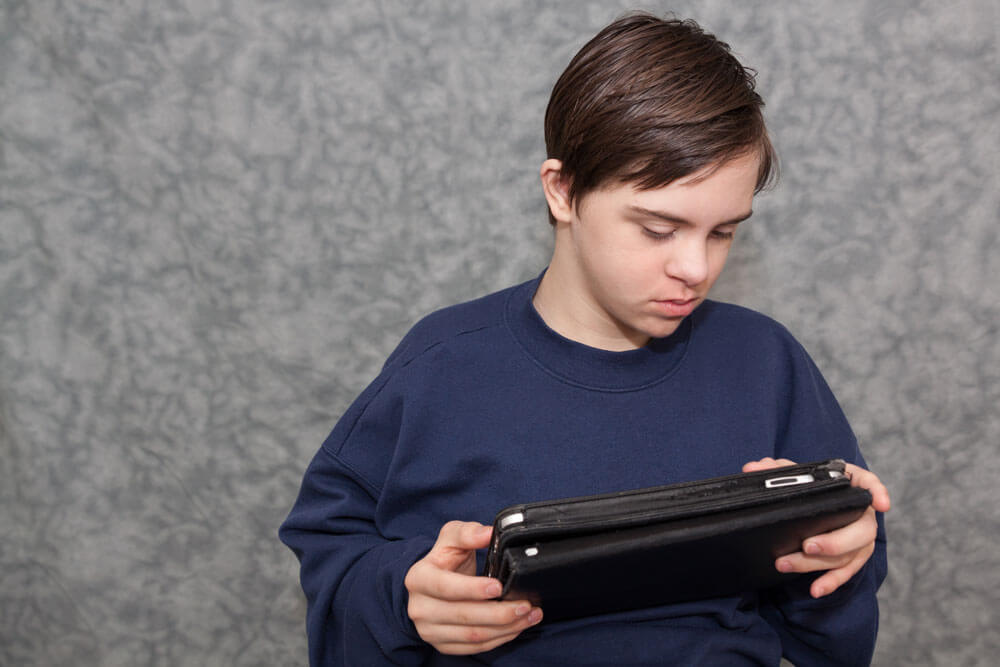 an adolescent holding and looking at a tablet device