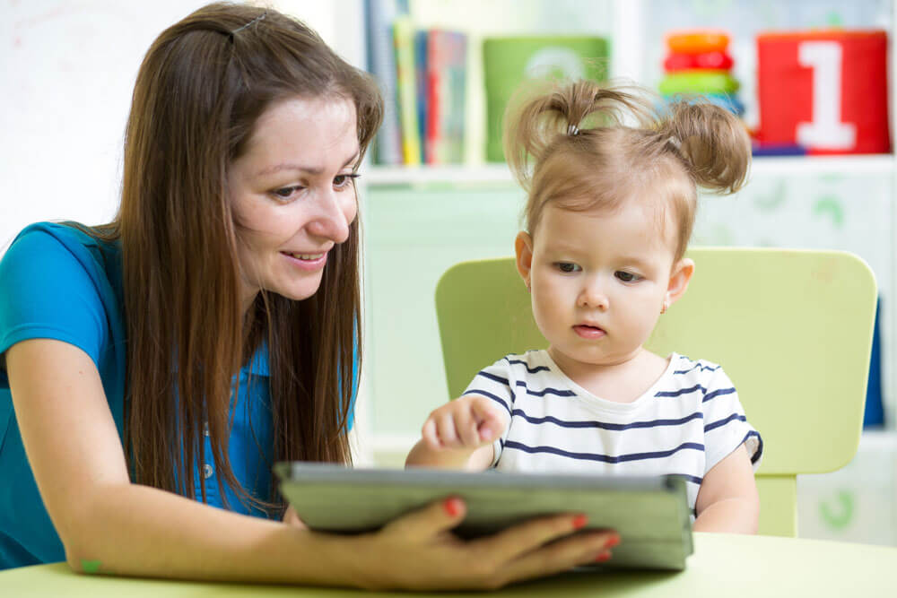 an adult and preschooler sitting together at a table looking at a tablet device