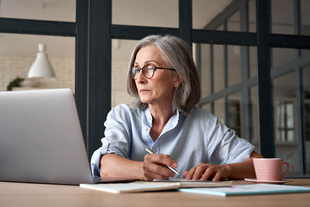 a person sitting at a table in an office looking at a laptop while taking notes